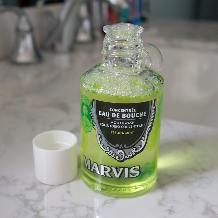 Open bottle of mouthwash with bubbles, resting on bathroom sink.