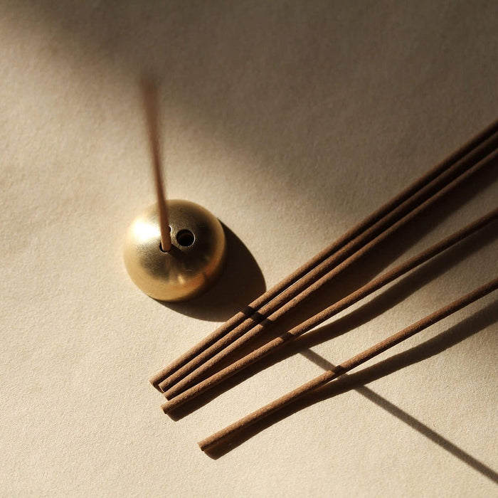 Gold incense burner with incense sticks on a beige background