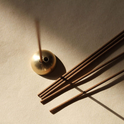 Gold incense burner with incense sticks on a beige background