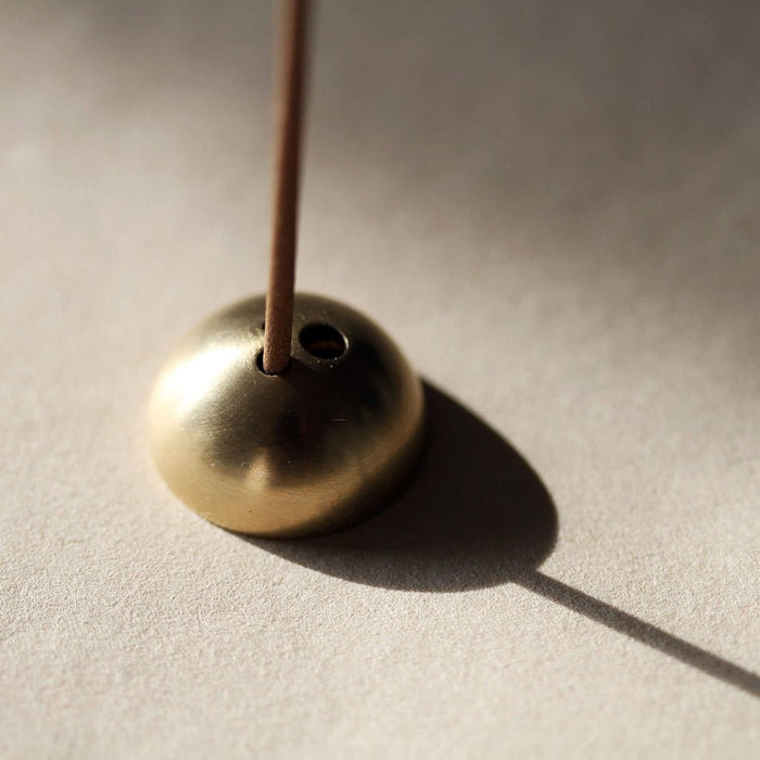 Brass incense holder with a single stick of incense on a neutral background