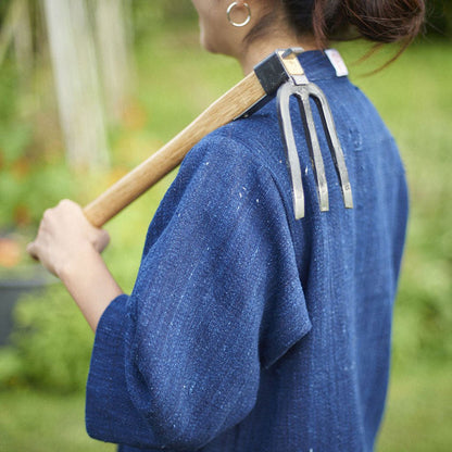 Person wearing a blue denim jacket holding a garden tool outdoors