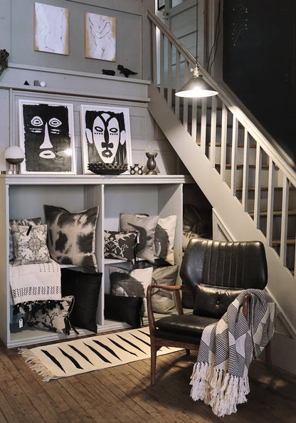 A black and white corner of a room with pillows on shelving and a staircase.
