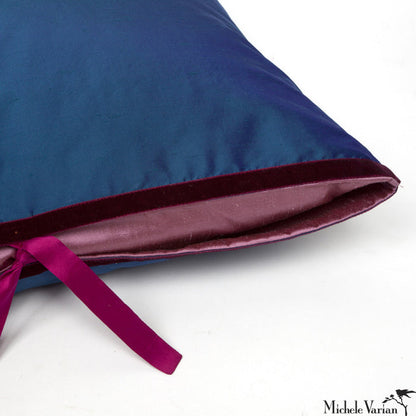 The top corner of a deep blue silk throw pillow with a silk lavender insert flap and silk fuchsia ties.